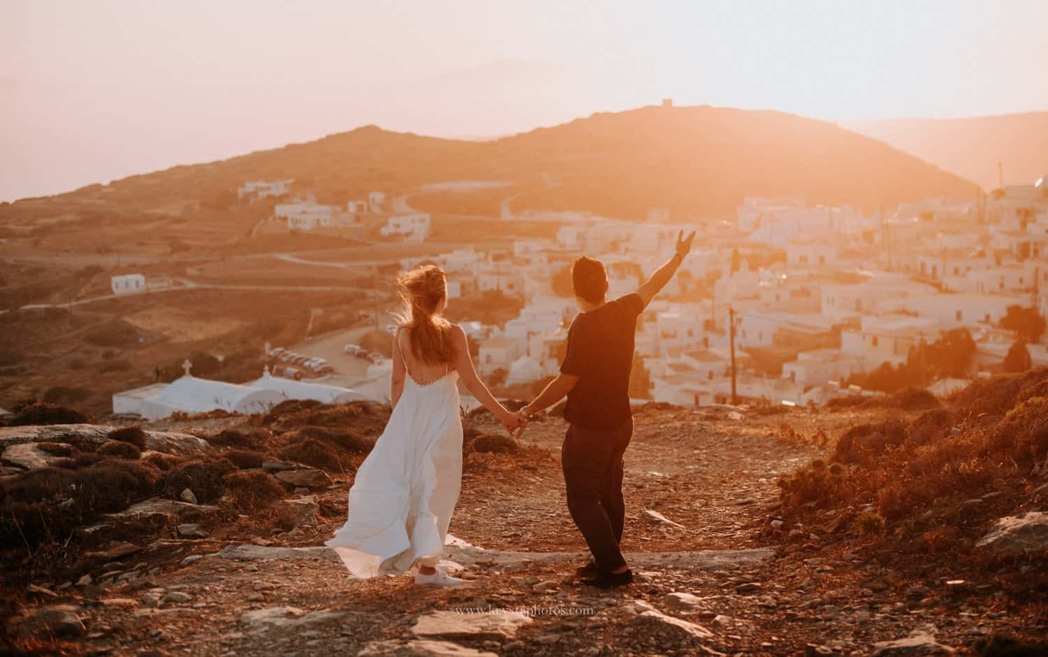 Couple holding hands at sunset overlooking the whitewashed village of Amorgos, Greece during a romantic engagement session